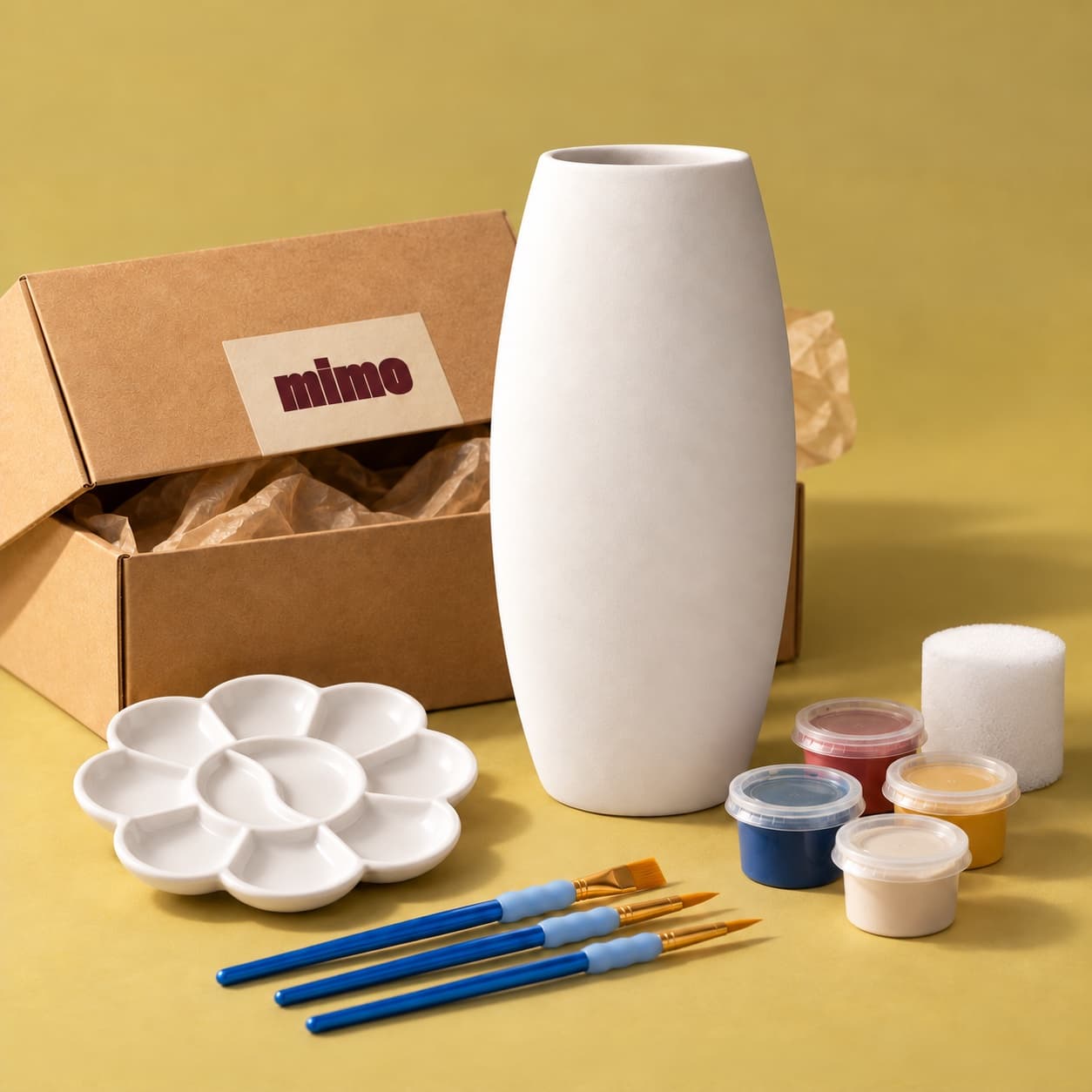 Kit MiMo avec un vase Naxos à peindre, une boîte kraft, des pots de peinture, des pinceaux, une palette et une éponge sur fond jaune