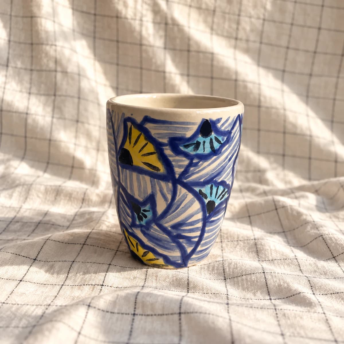 Gobelet peint de feuillages bleus et jaunes sur un fond clair