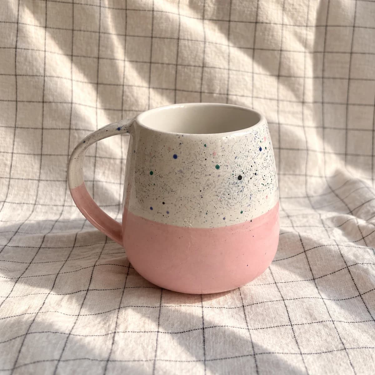 Mug rose et blanc moucheté posé sur un tissu clair quadrillé