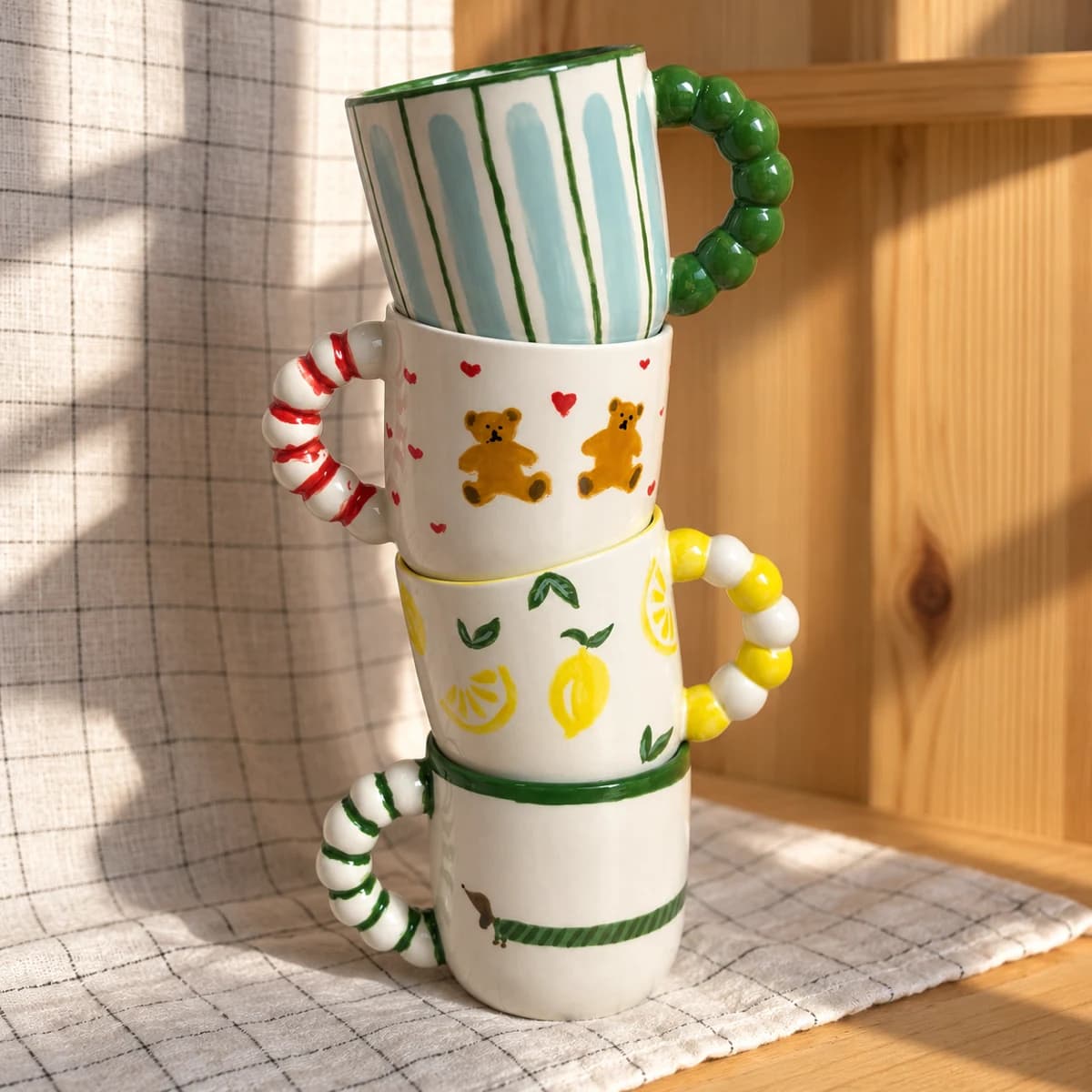 Quatre mugs peints à la main empilés, décorés de rayures, d’oursons, de citrons et d’un teckel
